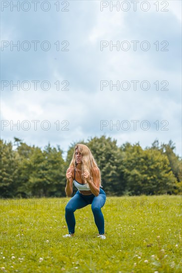 Fitness session with a young blonde caucasian woman exercising in nature with a blue maya on her feet and a white short shirt. Squatting and jumping