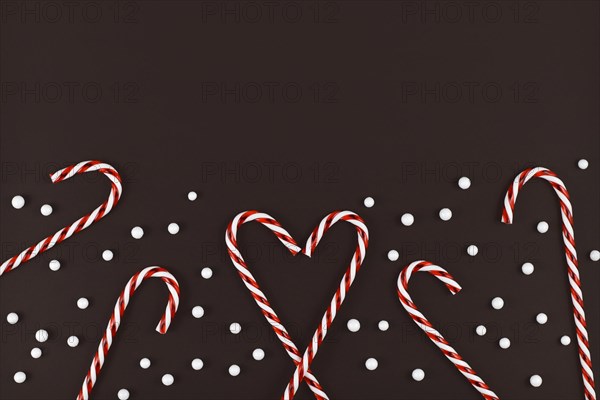 Christmas candy canes forming heart surrounded by white snowball ornaments on dark background
