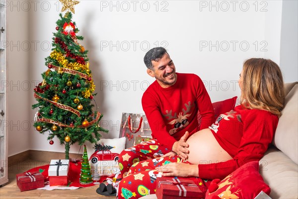 Young couple with decoration and red Christmas clothes touching the baby's bumps on the tummy. Family with pregnant woman