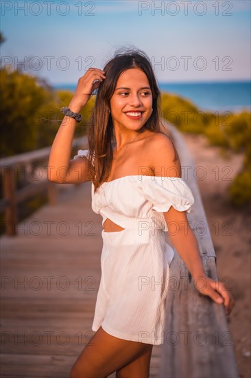 A young brunette caucasian on vacation at the beach in a white dress in summer
