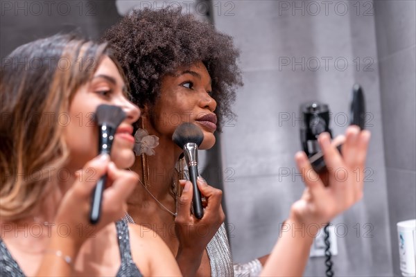 A young black girl with afro hair and a blonde Caucasian girl putting on makeup before the party with a smile. Exclusive party