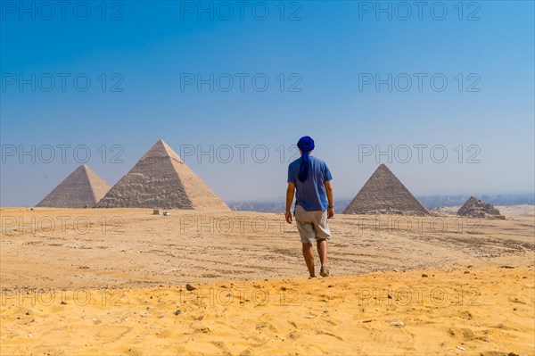 A young man in a blue turban walking next to the Pyramids of Giza