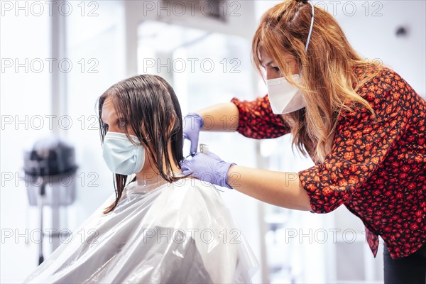 Hairdresser with mask and gloves cutting the ends with scissors to the client. Reopening with security measures for hairdressers in the Covid-19 pandemic