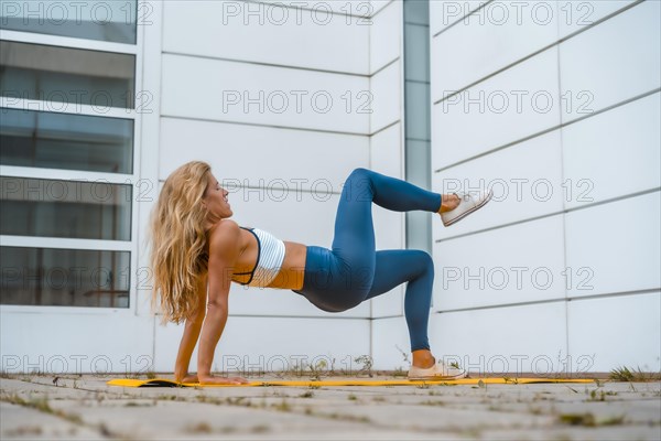 Fitness with blonde caucasian girl exercising on a yellow mat with white wall in the background