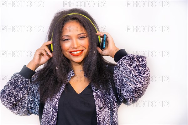 A portrait of a smiling Hispanic attractive woman on headphones holding a phone and choosing a song to play