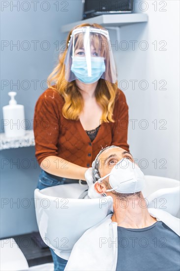 Reopening of hairdressing salons after the Coronavirus pandemic. Hairdresser with face mask and protective screen