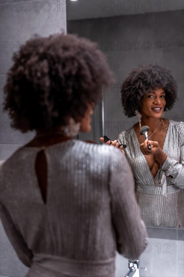 A young black girl with afro hair putting on makeup before the party with a smile. Exclusive party