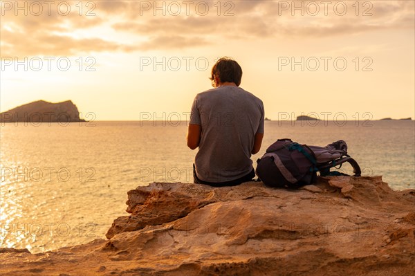 A tourist sitting watching the sunset at Cala Comte beach on the island of Ibiza. Balearic