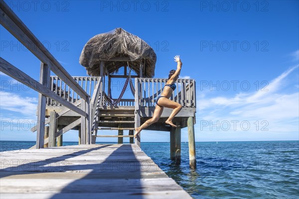 A young tourist girl throwing herself into the Caribbean Sea on Roatan Island from a wooden pier. Honduras