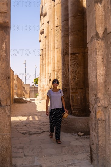 A young tourist in a white t-shirt and hat visiting the temple and looking at the ancient egyptian drawings on the columns of the Luxor Temple