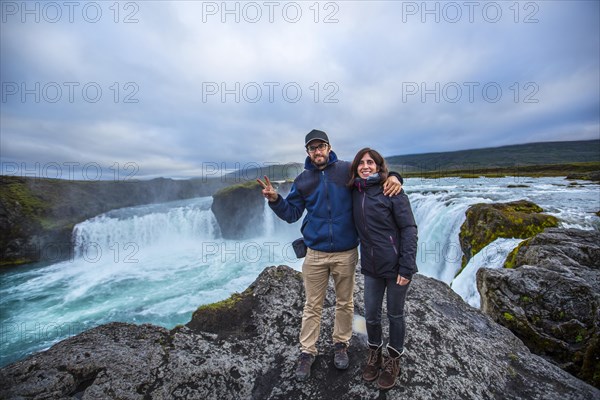 A young couple tourist looking at the Godafoss waterfall from above. Iceland