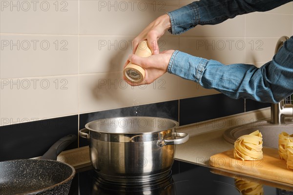 Unrecognizable woman adds salt to water boiling in saucepan on an induction stove