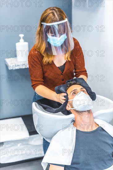 Reopening of hairdressing salons after the Coronavirus pandemic. Hairdresser with face mask and protective screen