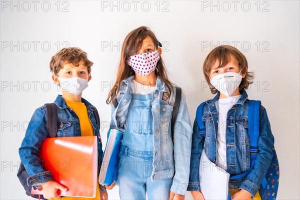 Three children with face masks ready to go back to school. New normality