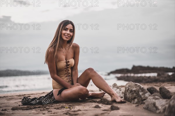 Fashion posing of a brunette woman in a swimsuit and a pareo on the beach in summer