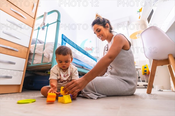 Young Caucasian mother playing with her in the room with toys. Baby less than a year learning the first lessons of her mother. Mother playing with her son playing sitting on the floor