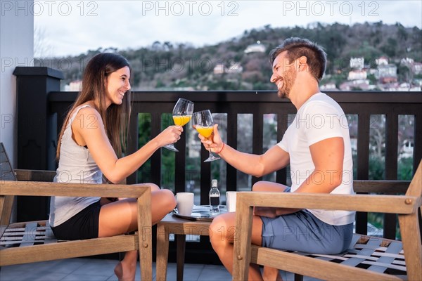 A Caucasian couple having breakfast on the hotel terrace in pajamas. Toasting with orange juice in the morning