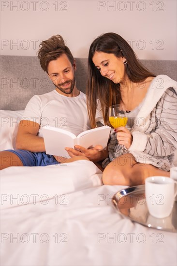 A couple in pajamas reading a book in the breakfast of coffee and orange juice in the hotel bed