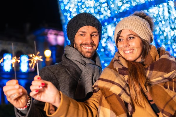 Winter portrait of a Caucasian couple enjoying the Christmas lights with torches in hand