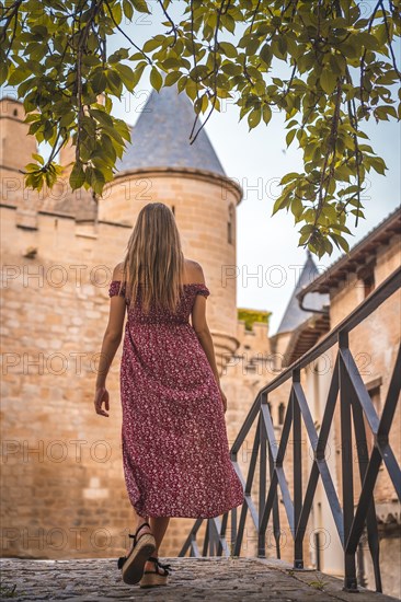 Blonde woman next to a medieval castle with a red dress from behind