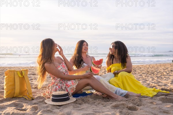 Idyllic summer picnic of three multi-ethnic friends enjoying together eating watermelon in the beach