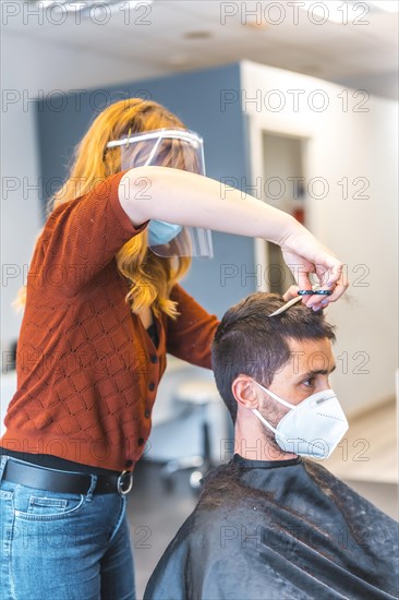 Hairdressers after the Coronavirus pandemic. Hairdresser with face mask and protective screen