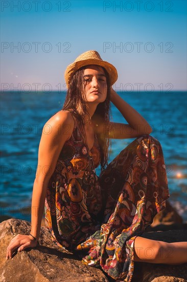 Portrait of a young Caucasian girl smiling with wet hair and a flower dress and a straw hat by the sea