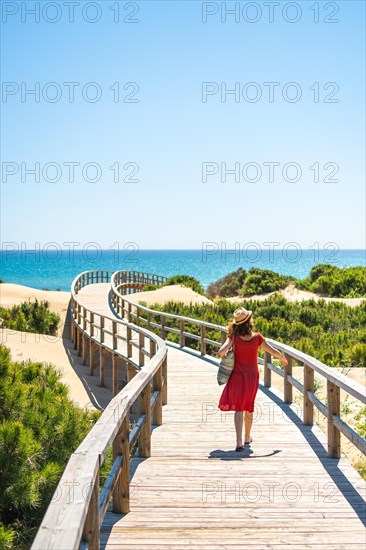 Girl with red dress on the wooden path to Playa Moncayo in Guardamar del Segura next to Torrevieja
