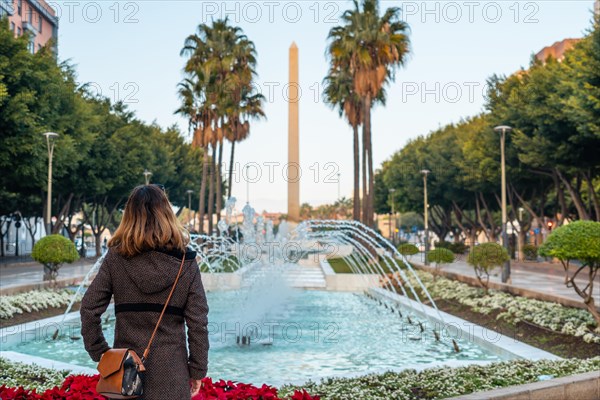 A young woman looking at the fountain of water and flowers next to the palm trees in the Belen street of the Rambla de Almeria
