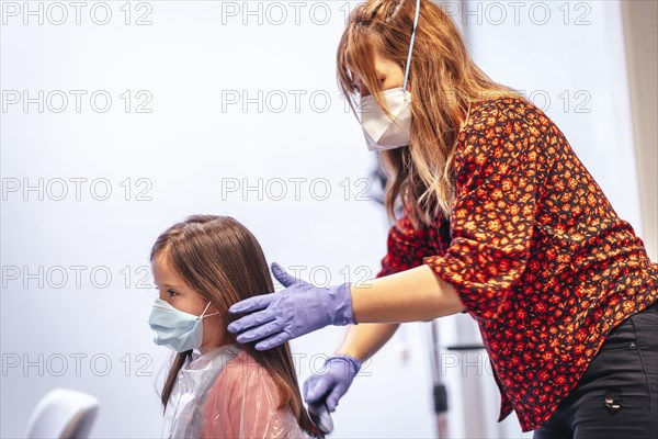 Hairdresser with mask and gloves combing the straight hair of a blonde girl