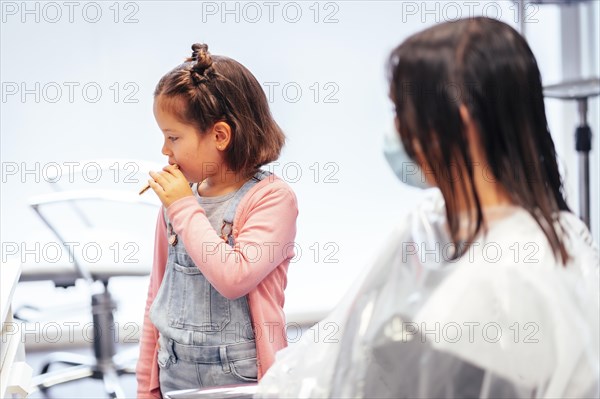 Client sitting waiting for the dye to dry and winged her daughter eating a cookie. Reopening with security measures for hairdressers in the Covid-19 pandemic