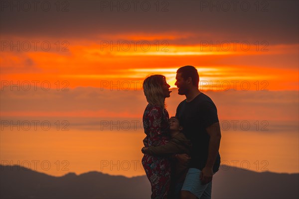 Parents on the top of a mountain at sunset and his son watching them