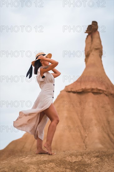 Brunette Caucasian model with a white dress and a straw hat in the Castildetierra of the Bardenas Reales desert