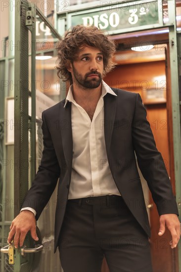 Street style with a young dark-haired caucasian man in a black suit and a white shirt in a luxurious hotel