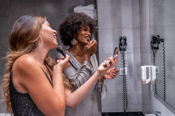 A young black girl with afro hair and a blonde Caucasian girl putting on makeup before the party with a smile. Exclusive party