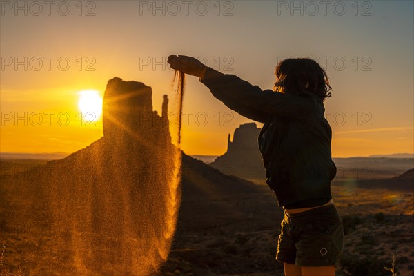 A brunette lifestyle girl at the dawn of Monument Valley throwing sand between her hands