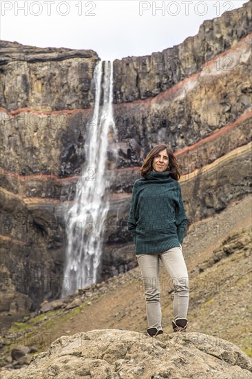 A young woman looking at the waterfall above Hengifoss from above. Iceland
