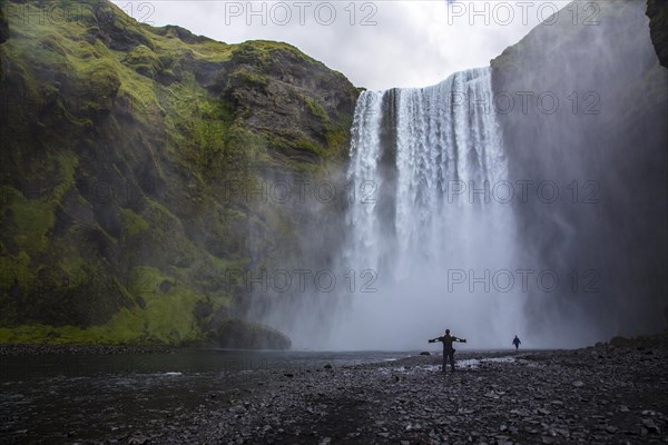 A tourist with open arms at the bottom of the Skogafoss waterfall in the golden circle of the south of Iceland