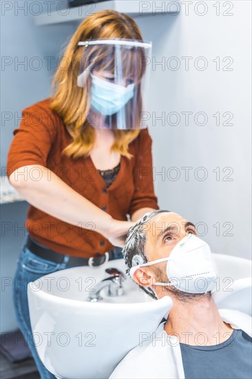 Hairdressers after the Coronavirus pandemic. Caucasian hairdresser with face mask and protective screen