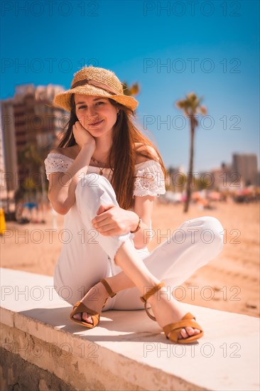 A Caucasian redhead dressed in white and with a straw hat on the beaches of Calpe