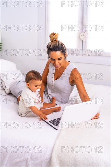 Young Caucasian mother with her son in the room on top of the bed. Drink less than a year in a video call with her family. Communication with grandparents in the confinement of the covid-19 pandemic