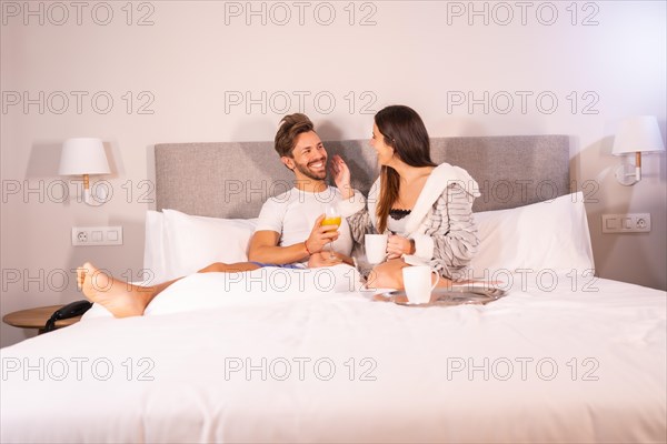 A loving couple in pajamas having coffee and orange juice for breakfast in the hotel bed in the morning