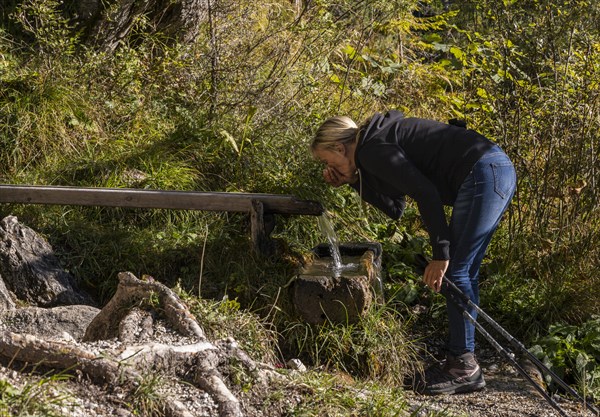 Hiker refreshes himself at the wooden fountain with spring water in Maria Alm