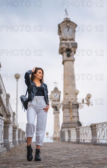 Lifestyle in the city with a blonde girl in white pants and a leather jacket. Walking down a slope with clocks in the background