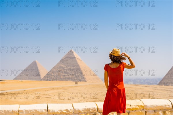 A young tourist in a red dress looking at the Pyramids of Giza