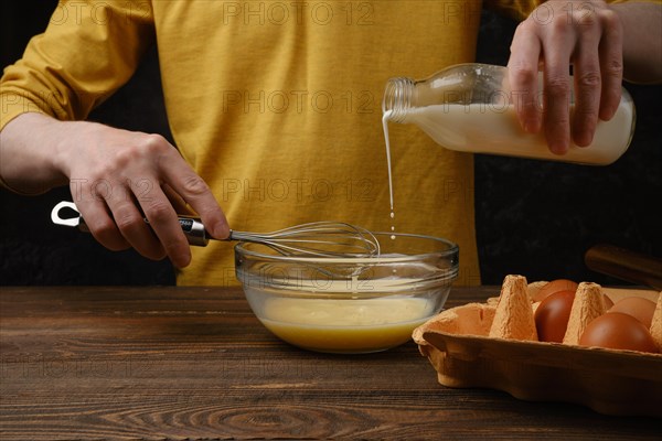 Pouring milk in a bowl with eggs for omelette