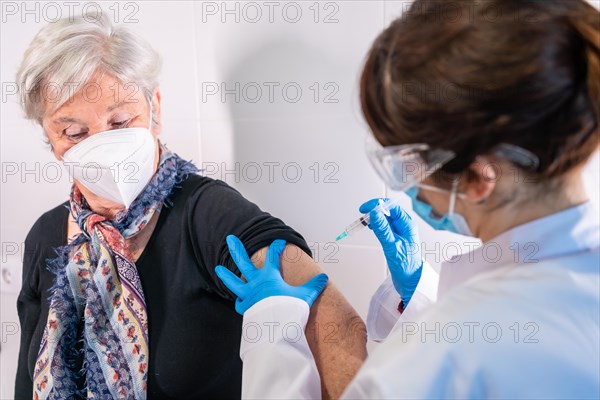 An elderly woman receiving the injection of the coronavirus vaccine by a doctor to receive the antibodies