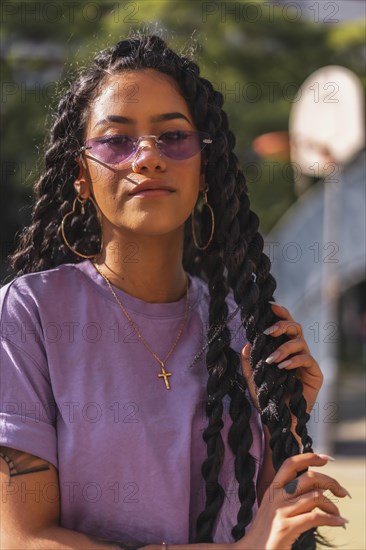 Dark-skinned young man in purple shirt holding long braids