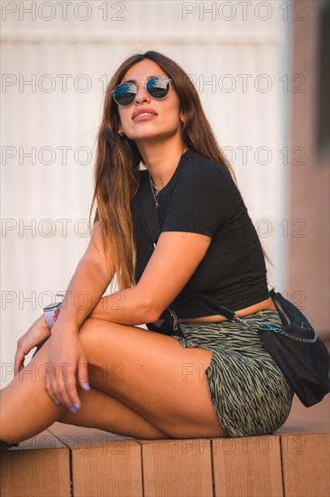 Street Style of an attractive young caucasian brunette sitting in the city with sunglasses