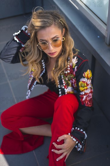 Fashion portrait of a blonde woman on a terrace sitting on the ground